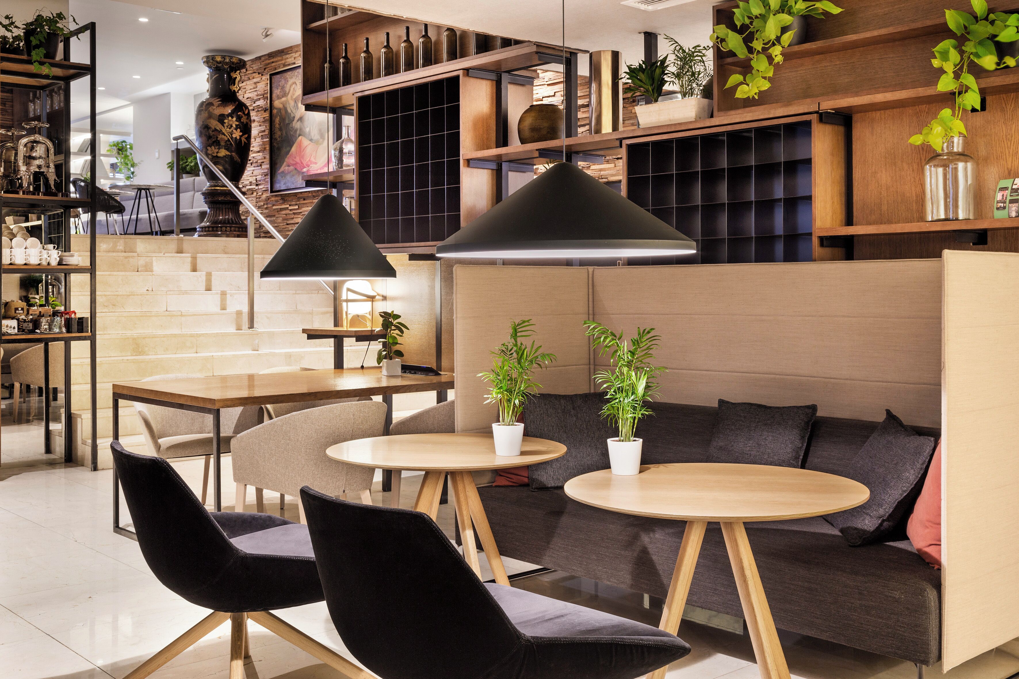 Ein modernes Interieur mit einer Holztreppe, runden Tischen, schwarzen Stühlen und einer Couch mit Kissen.