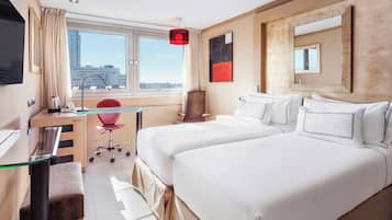 A hotel room with two beds, a desk, a chair, a TV, and a large window with a city view.