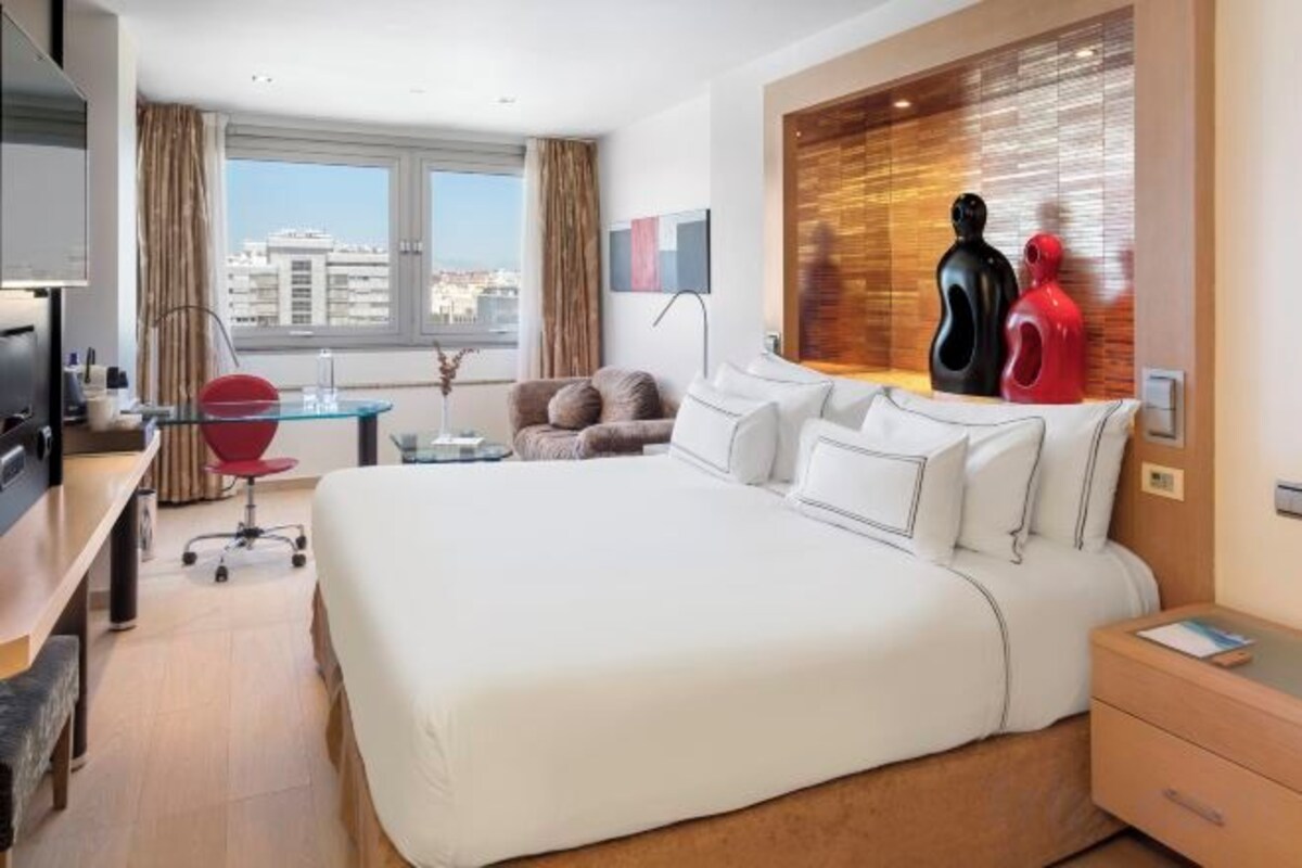 Une chambre d’hôtel avec un grand lit, un bureau avec une chaise, une télévision et une fenêtre donnant sur la ville.