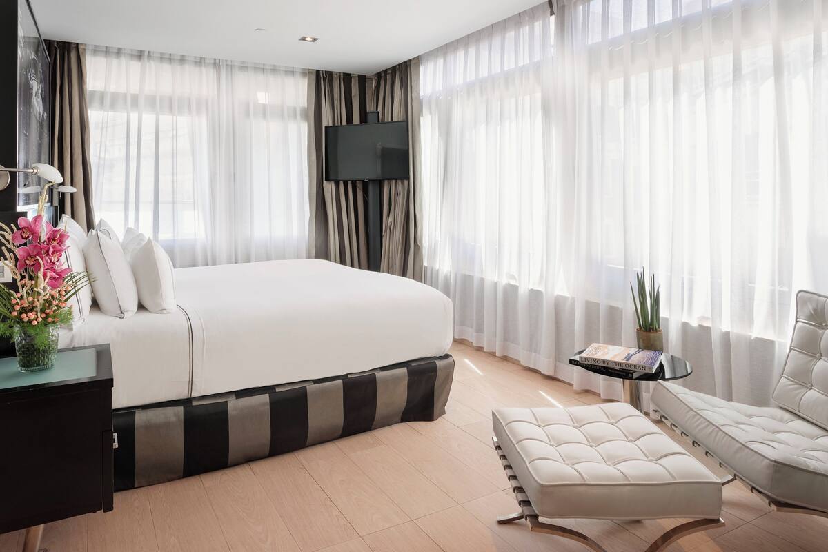 A modern hotel room with a large bed, a flat-screen TV, a sofa, and a small table with a book.
