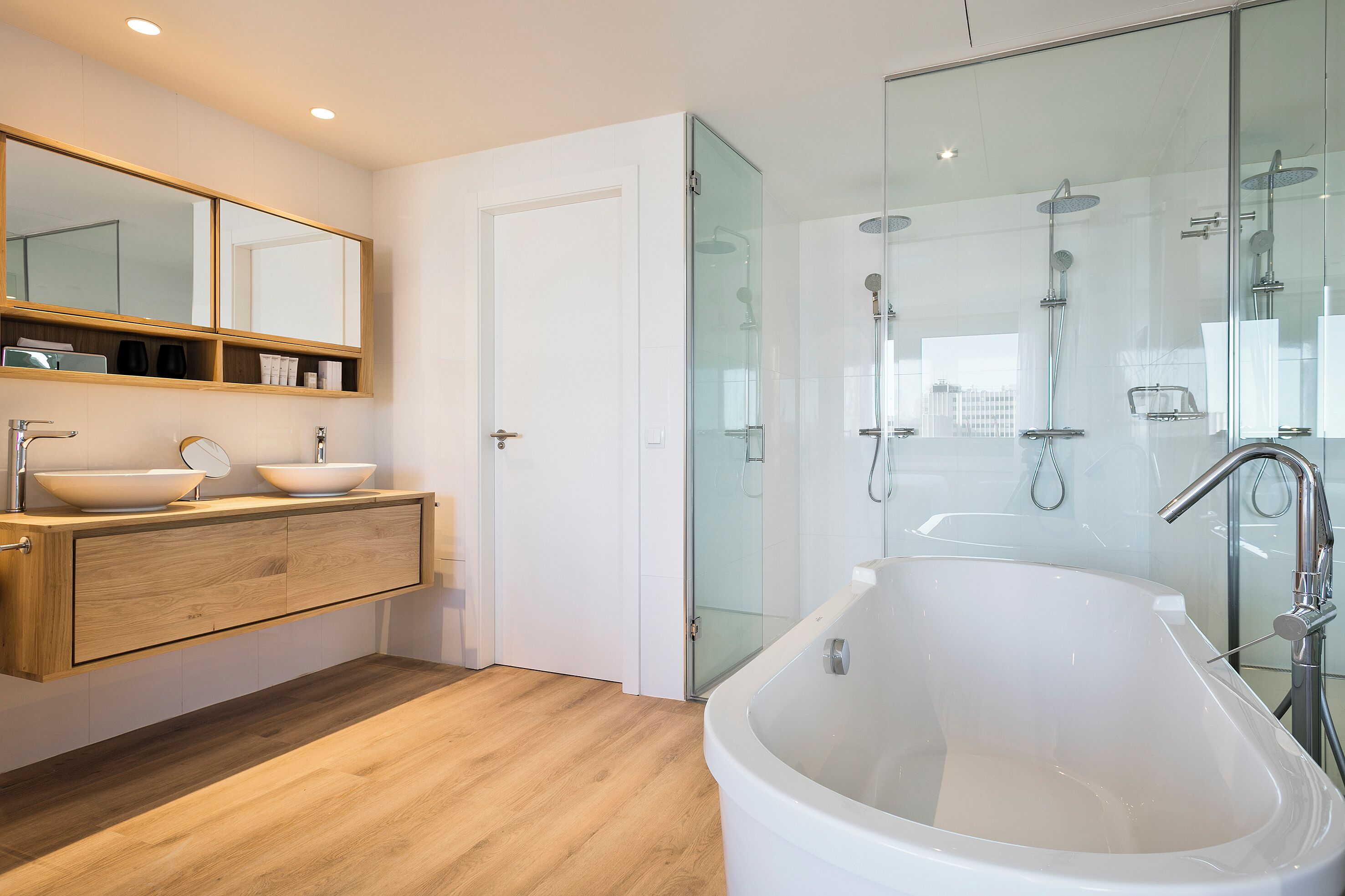 Un baño moderno con una bañera independiente, ducha con mampara de vidrio y un tocador con espejo y dos lavamanos.