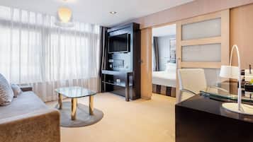 Een moderne hotelkamer met een bank, een glazen tafel, een televisie en een bureau met een lamp.