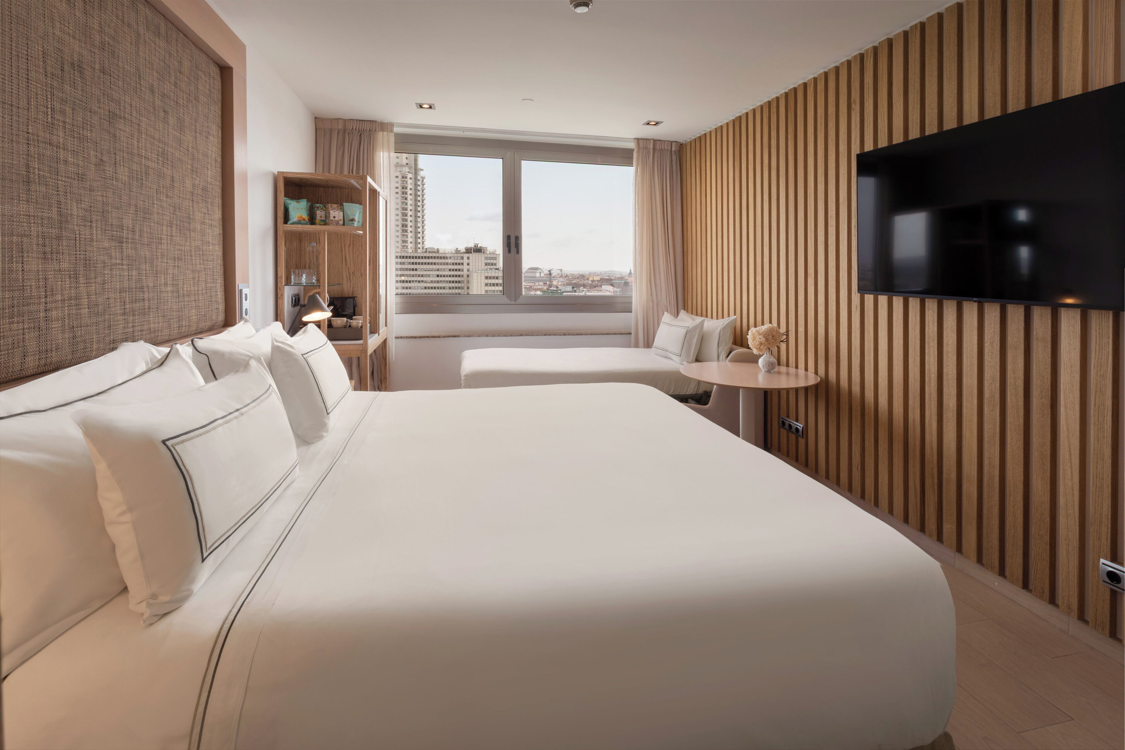 Habitación de hotel con una cama grande, televisión, una mesita y ventana con vistas a la ciudad.