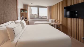Habitación de hotel con una cama grande, televisión, una mesita y ventana con vistas a la ciudad.