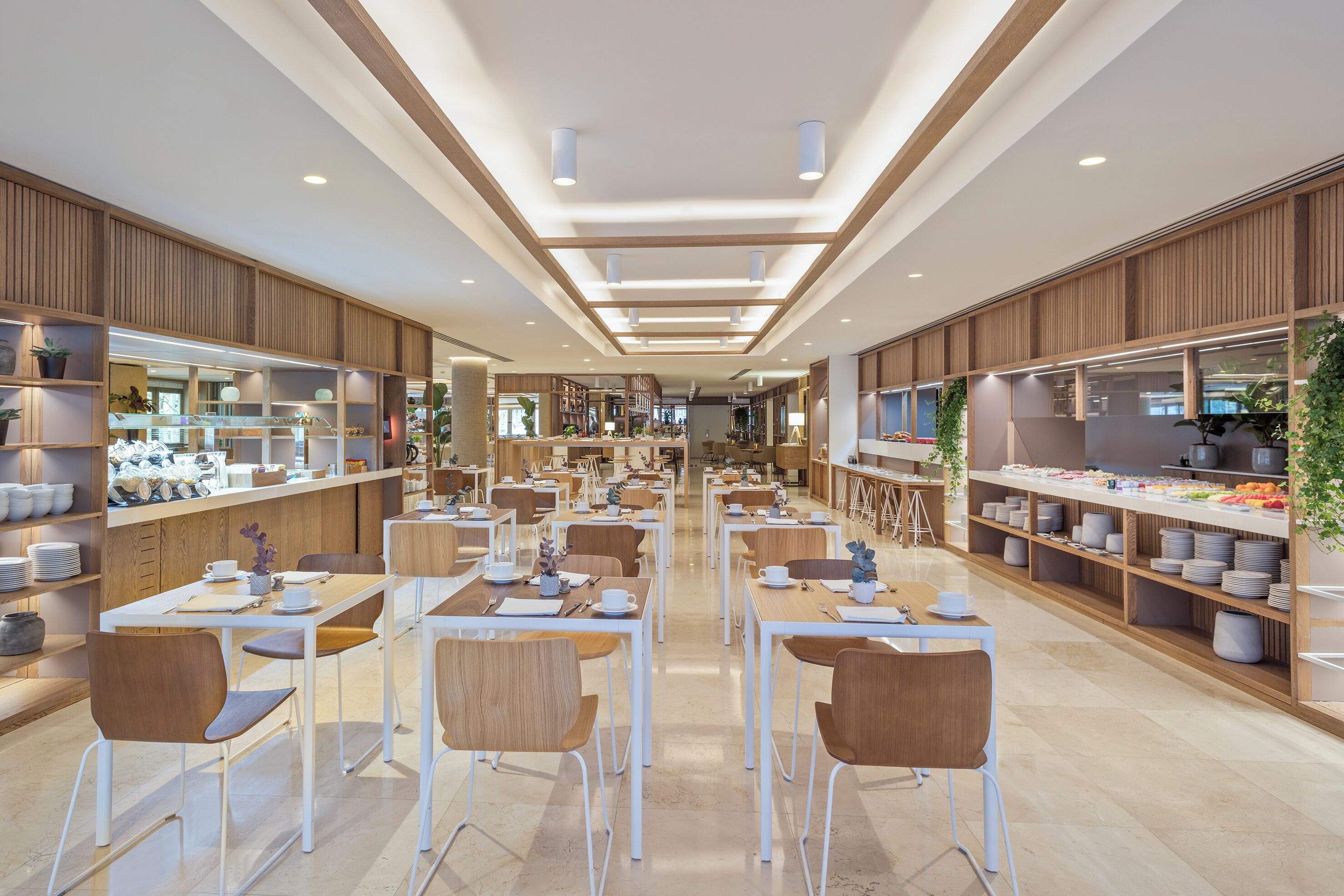 A spacious cafe with multiple tables and chairs, wooden paneling, and shelves stocked with various items.