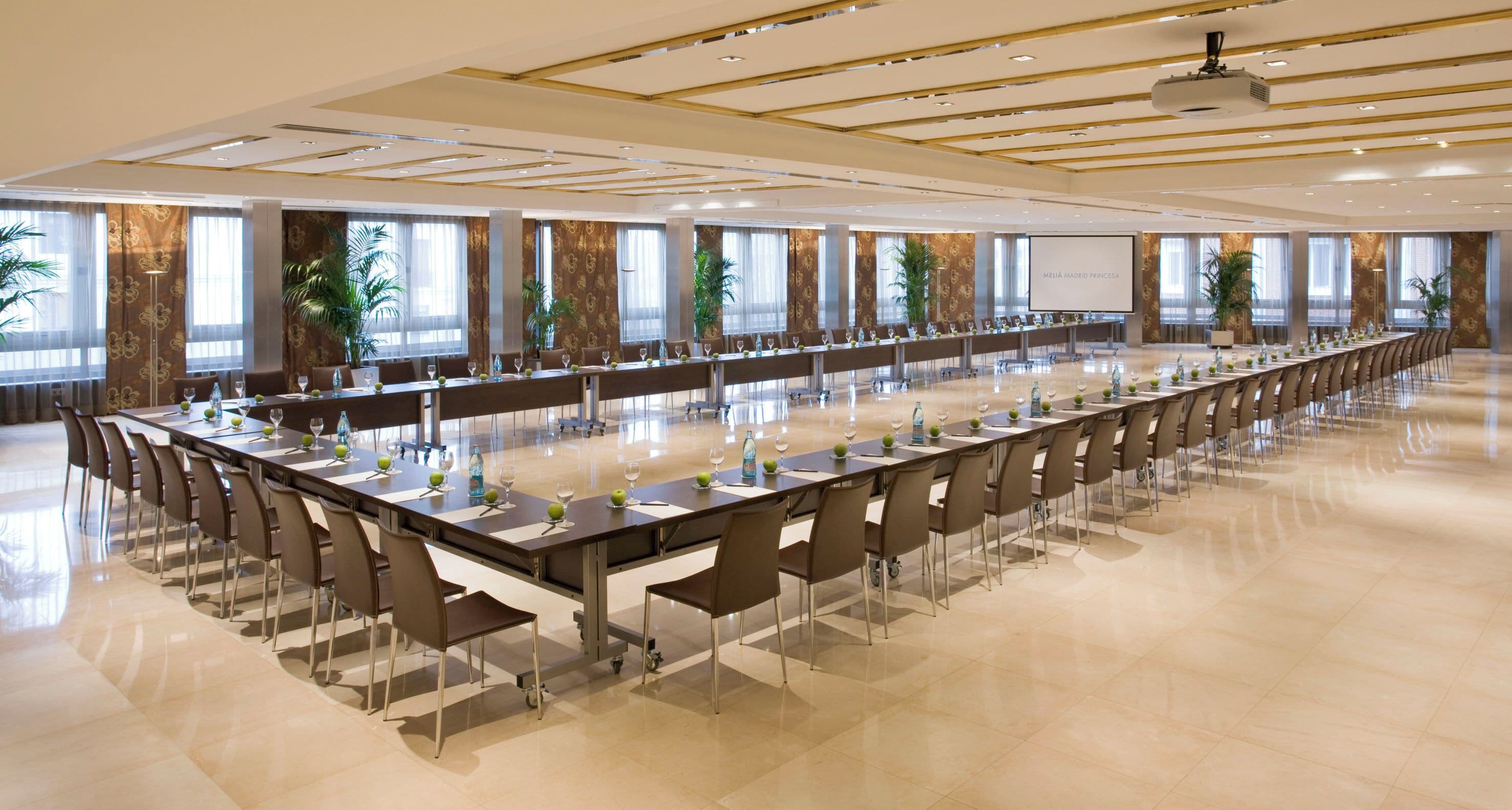 A conference room with long tables, chairs, and a projector screen.