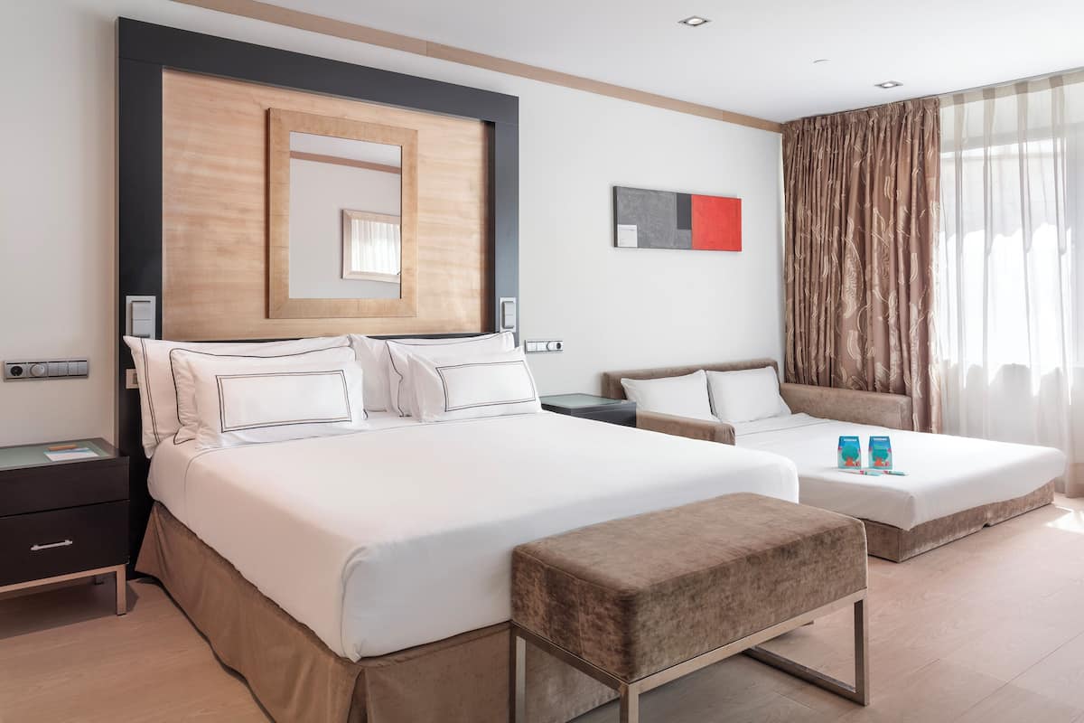 A hotel room with two beds, a large mirror, a bedside table, and a window with curtains.