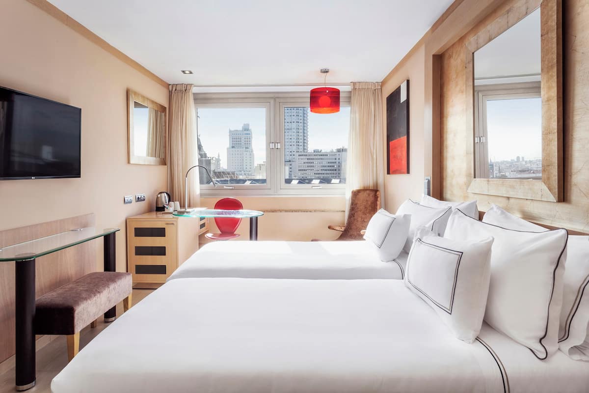 A hotel room with a bed, a desk, a chair, a TV, and a window with a city view.