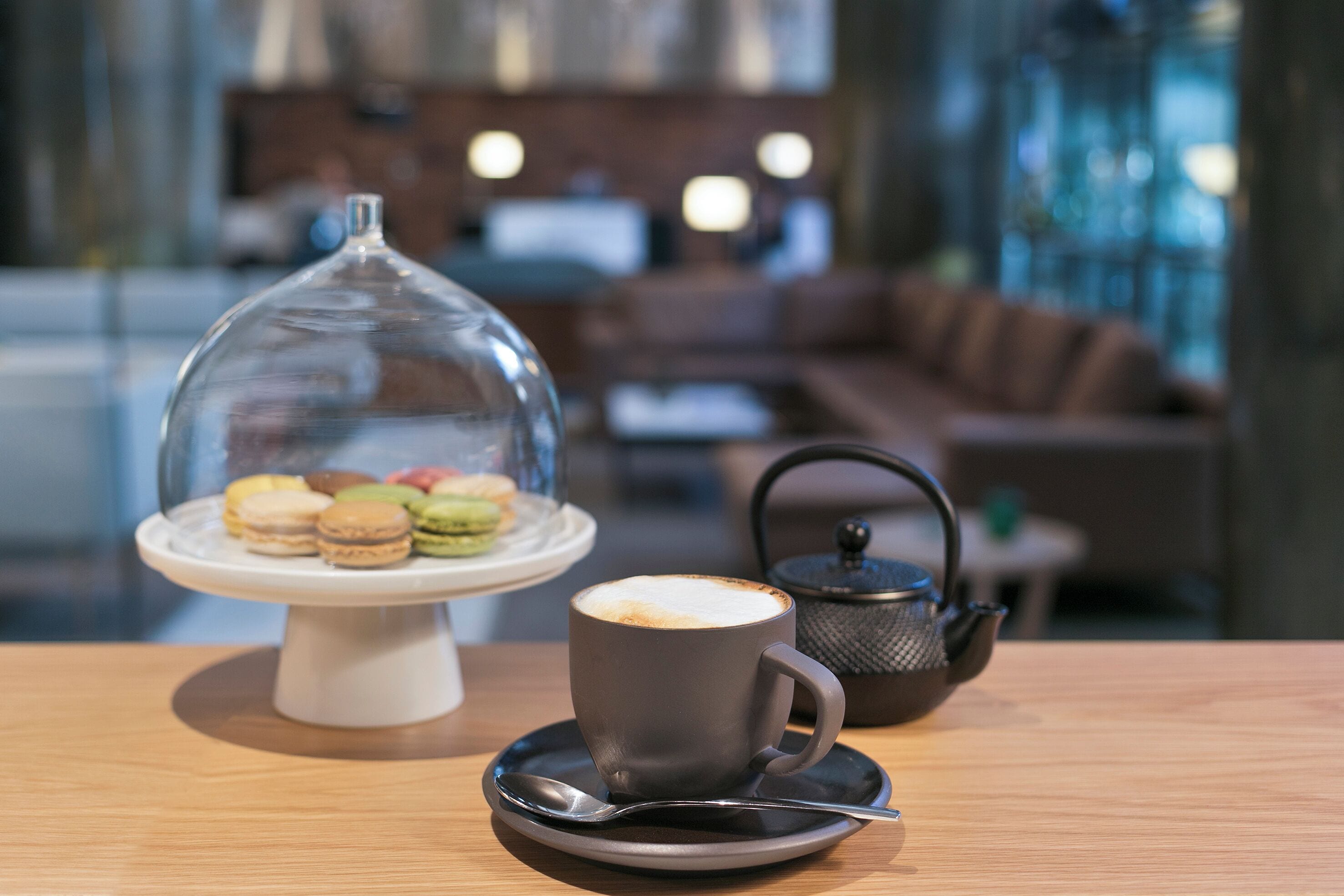 A table with a cup of coffee, a teapot, and a dessert display.
