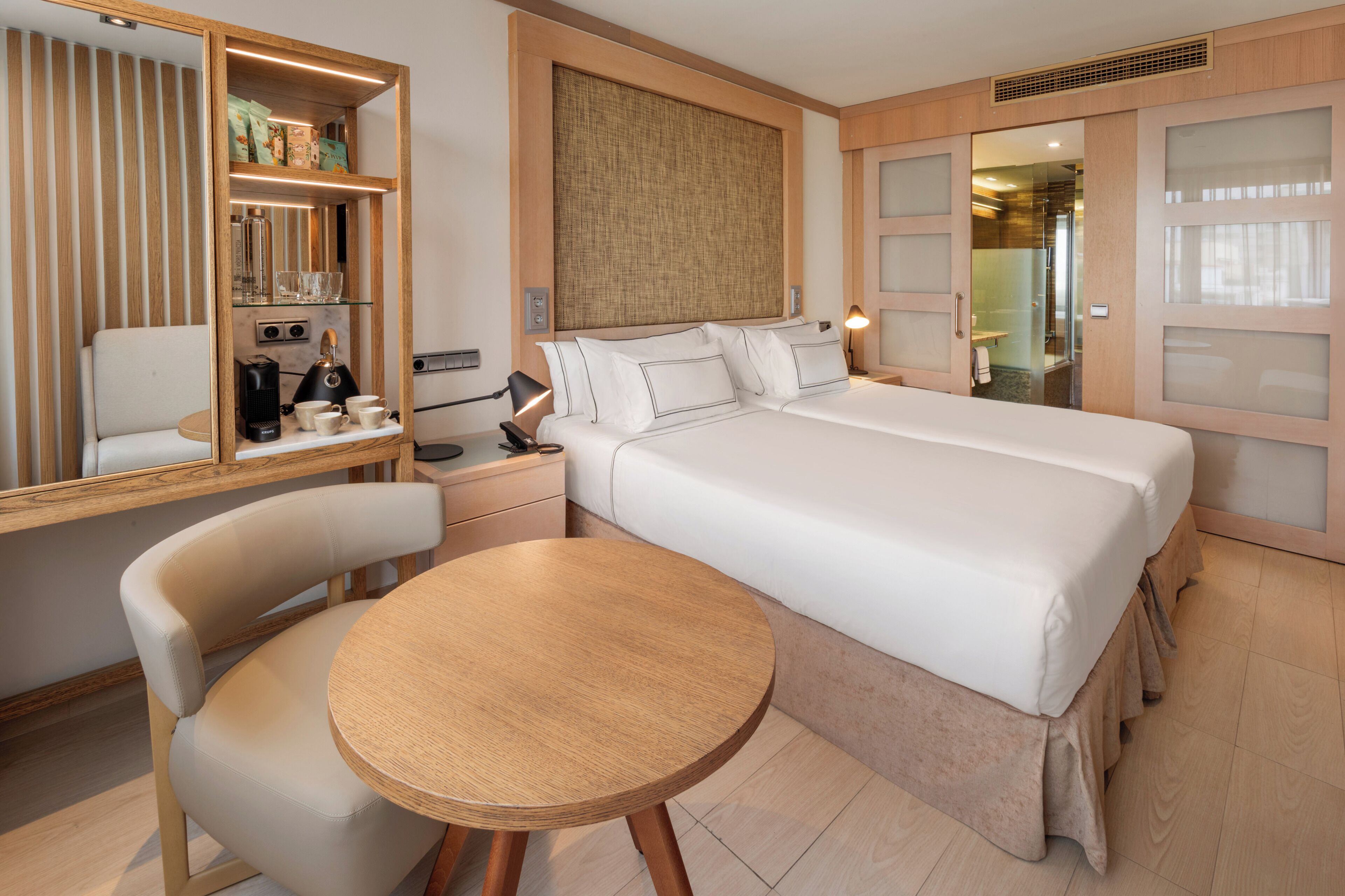 Habitación de hotel con cama, escritorio con silla, una mesita, armario y espejo.