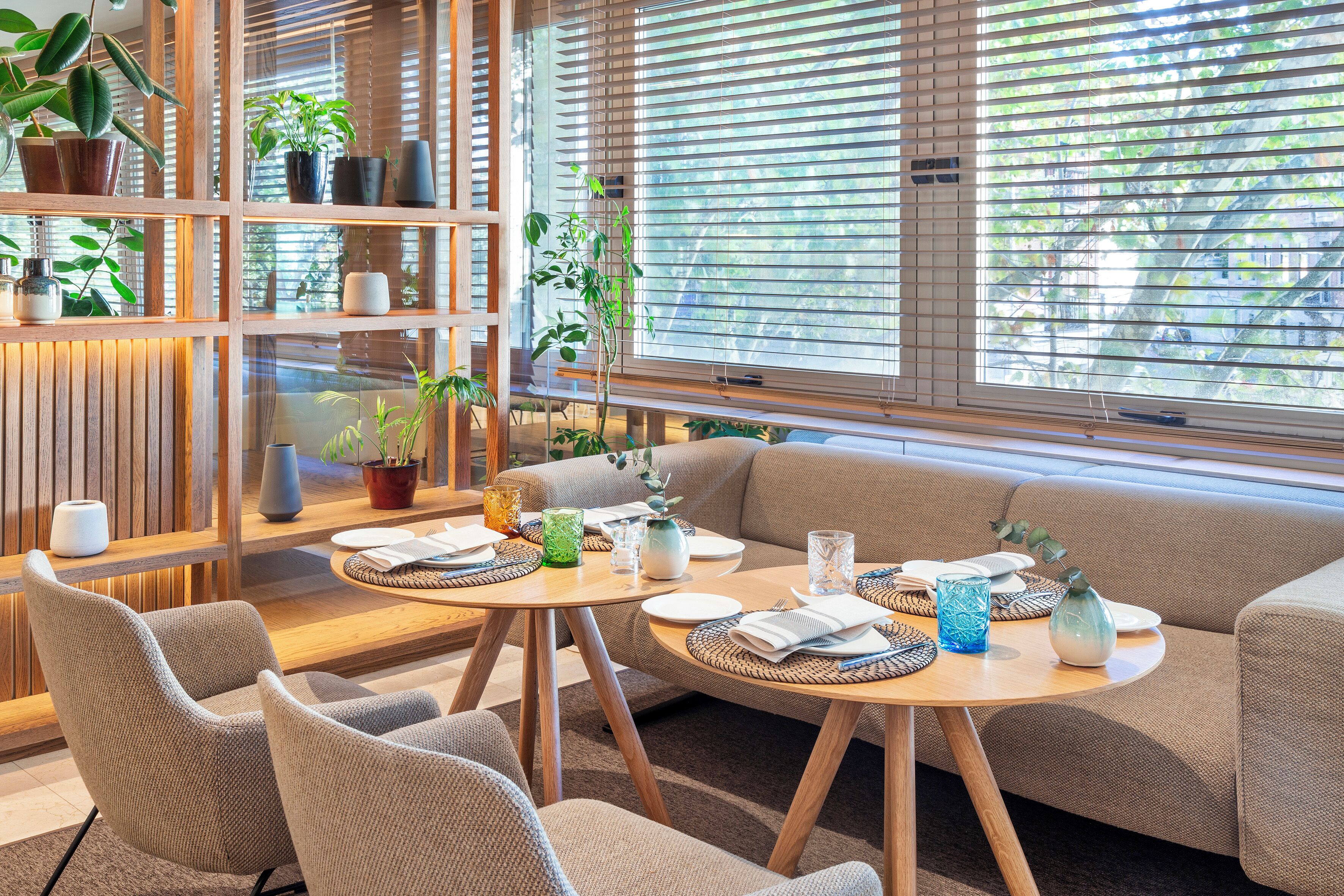 Una sala de estar moderna con un sofá, dos sillones, una mesa de centro de madera y una estantería con plantas en macetas.