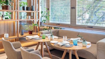 Una sala de estar moderna con un sofá, dos sillones, una mesa de centro de madera y una estantería con plantas en macetas.