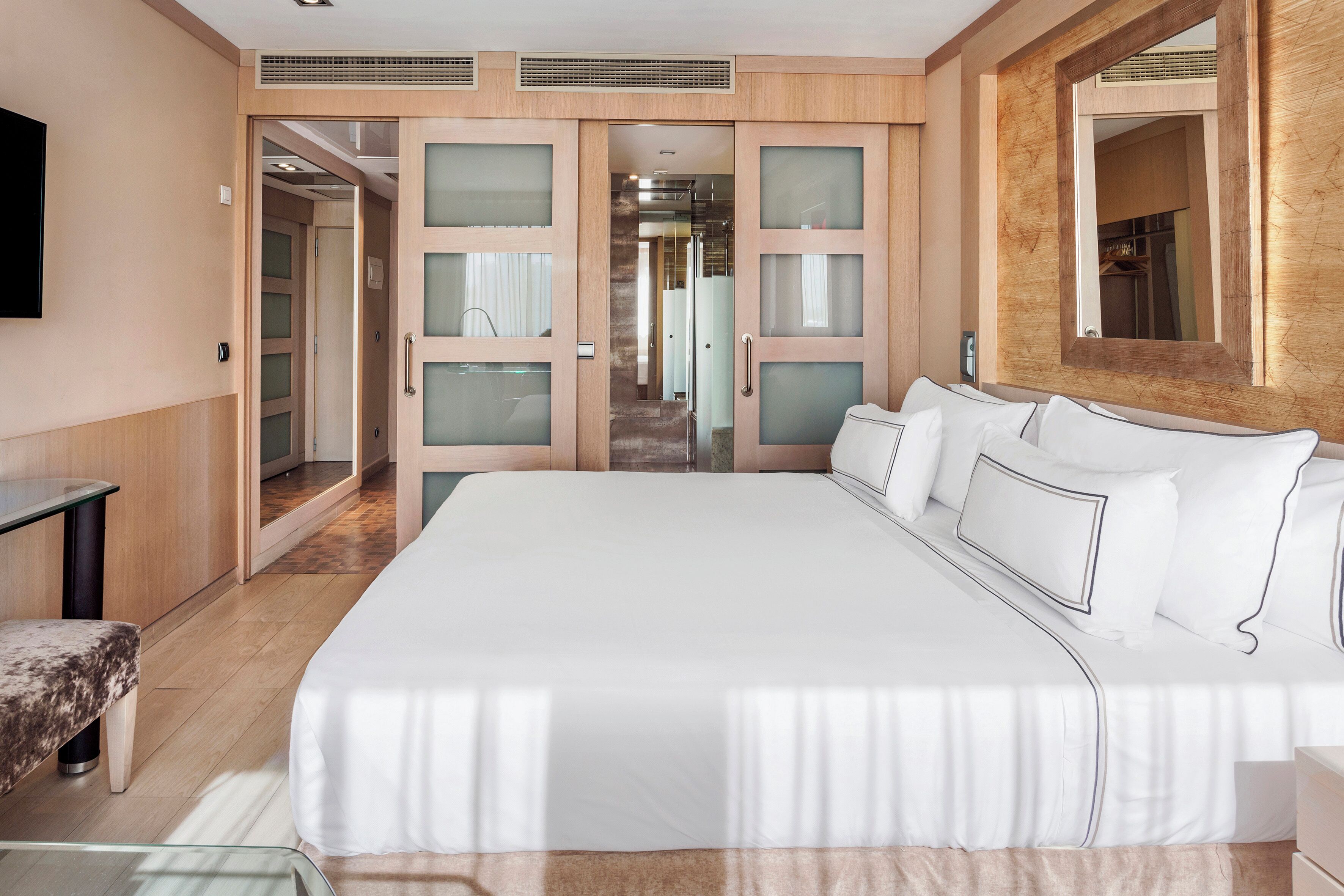 A modern hotel room with a large bed, a desk, and a mirror.