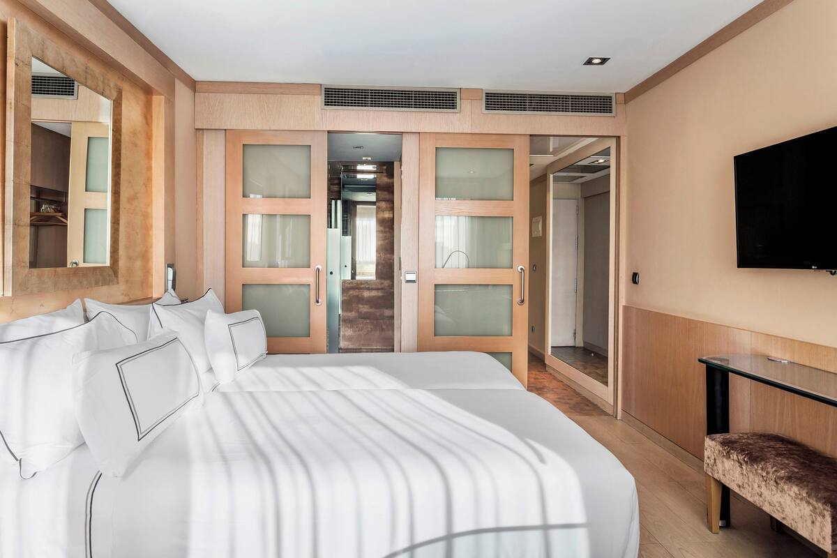A modern hotel room with a large bed, a TV mounted on the wall, and a walk-in closet with sliding doors.