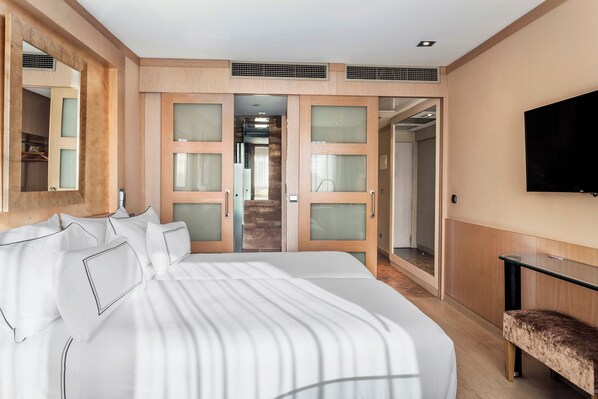 A modern hotel room with a large bed, a TV mounted on the wall, and a walk-in closet with sliding doors. - Melia Madrid Princesa (Madrid)