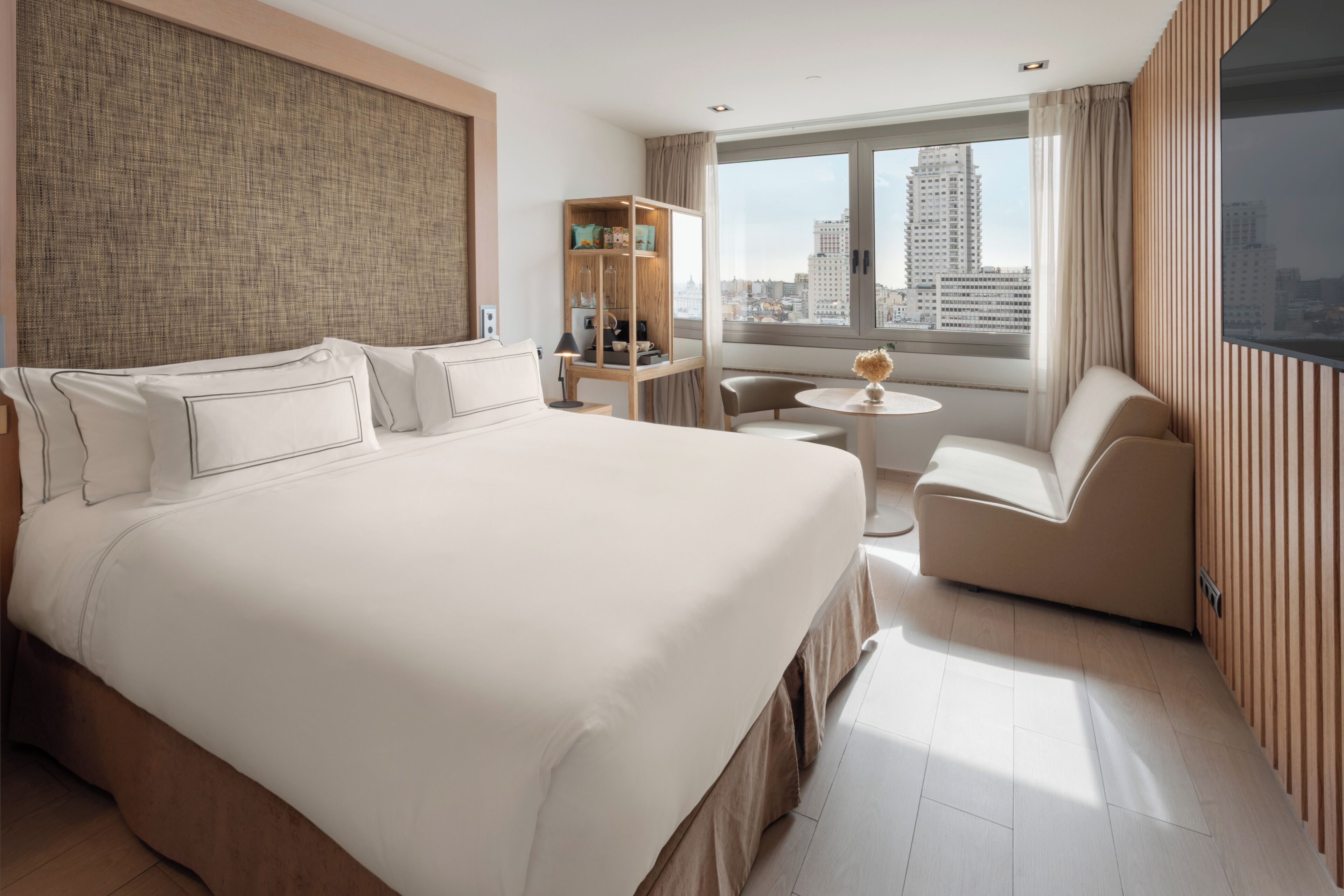 Une chambre d’hôtel avec un grand lit, un coin salon, une petite table et une vue sur la ville.