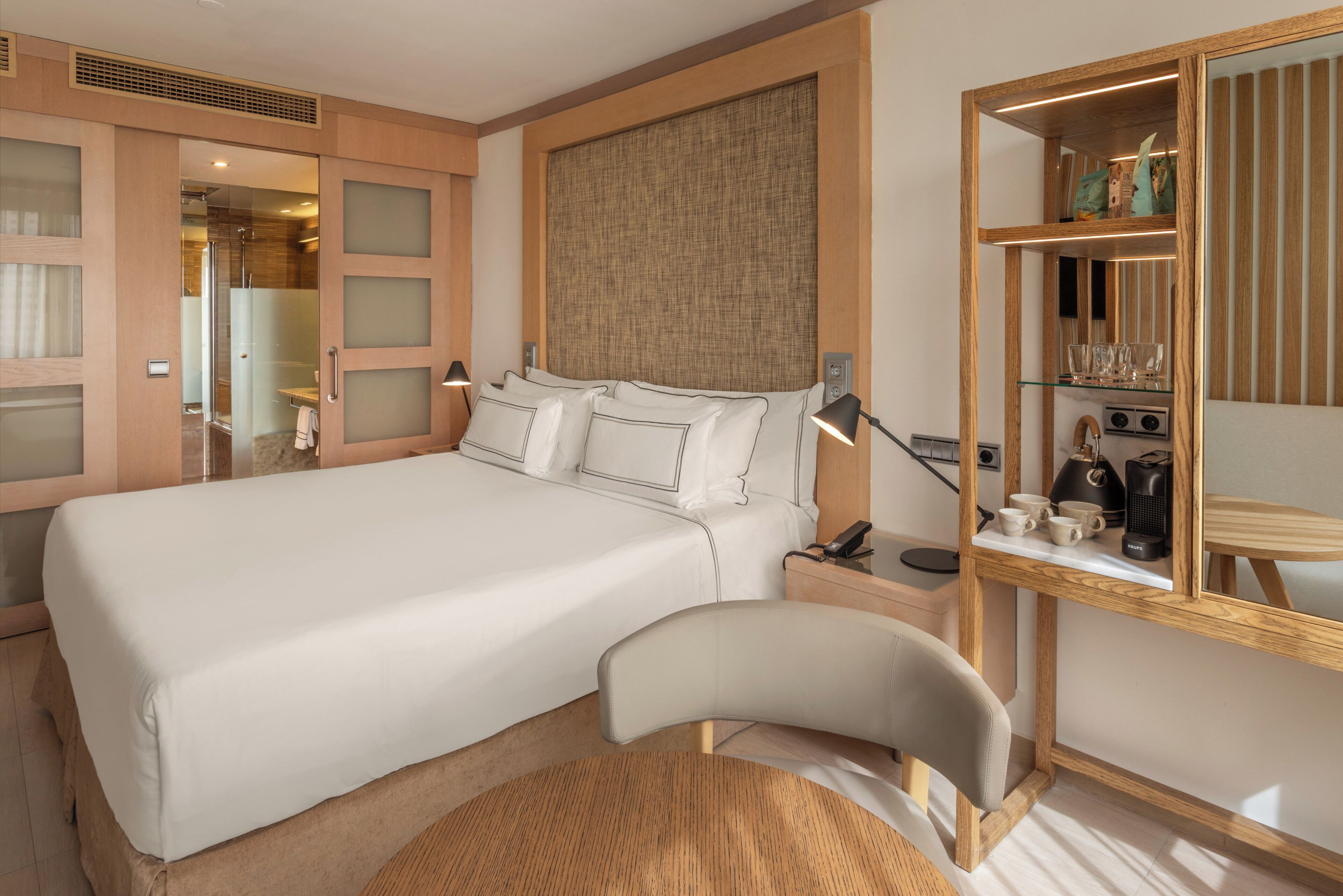 A hotel room with a large bed, bedside tables, a mirror, and a small seating area.