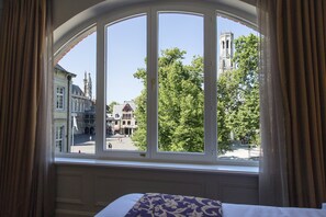 Enjoy a view of the historic town square from the comfort of this room, featuring a large arched window and a cozy bed with a patterned bedspread.