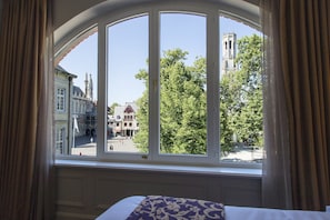 Enjoy a view of the historic town square from the comfort of this room, featuring a large arched window and a cozy bed with a patterned bedspread.