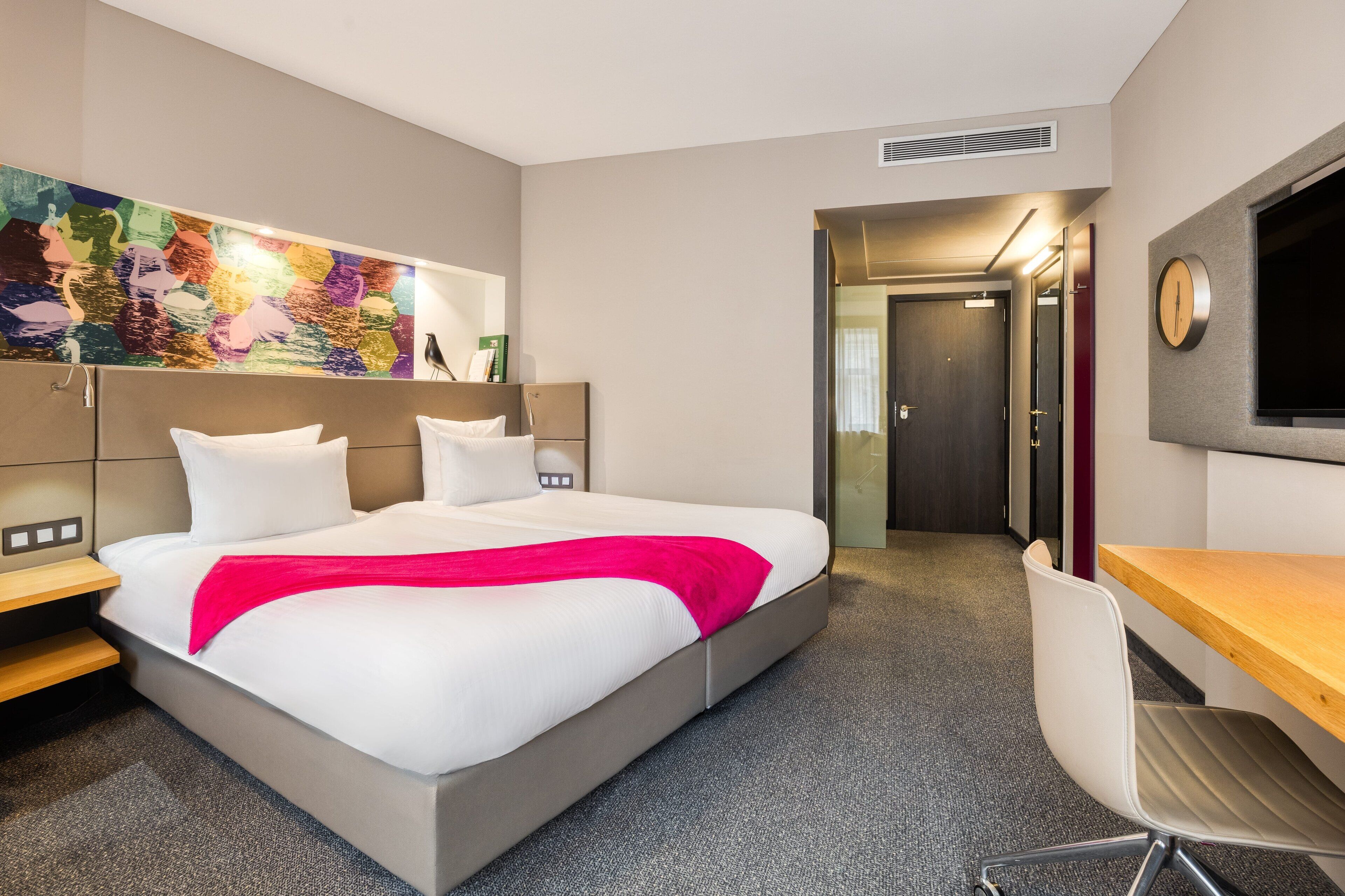 Una habitación de hotel moderna con una cama grande, un escritorio y una televisión.