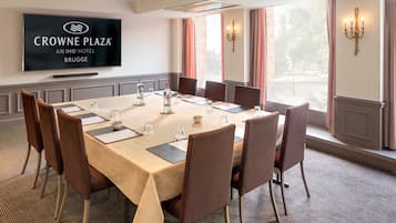 Een vergaderzaal met een lange tafel, stoelen, een flatscreen-tv en uitzicht op de omgeving.