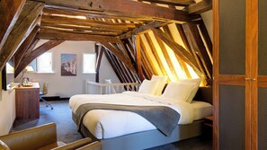 A bedroom with a sloped ceiling, a bed, a chair, and a desk with a lamp. - Crowne Plaza Bruges by IHG (Bruges)