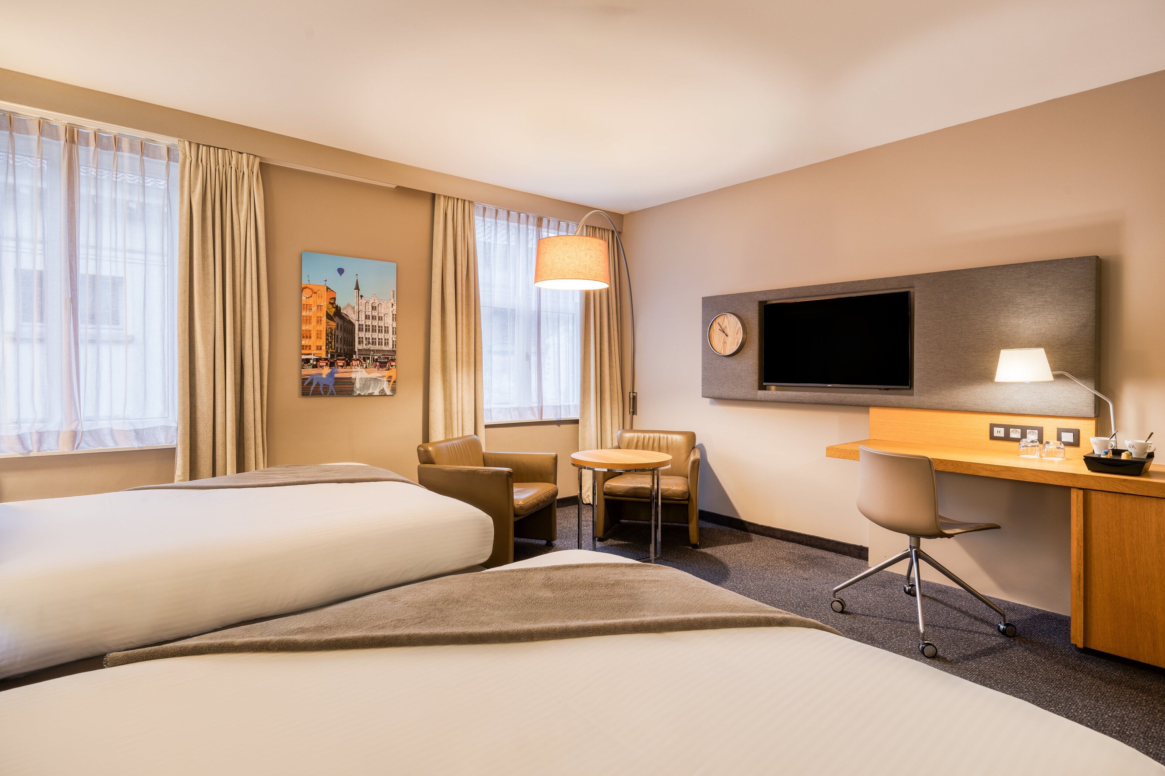 A hotel room with two beds, a desk, a chair, a television, and a painting on the wall.