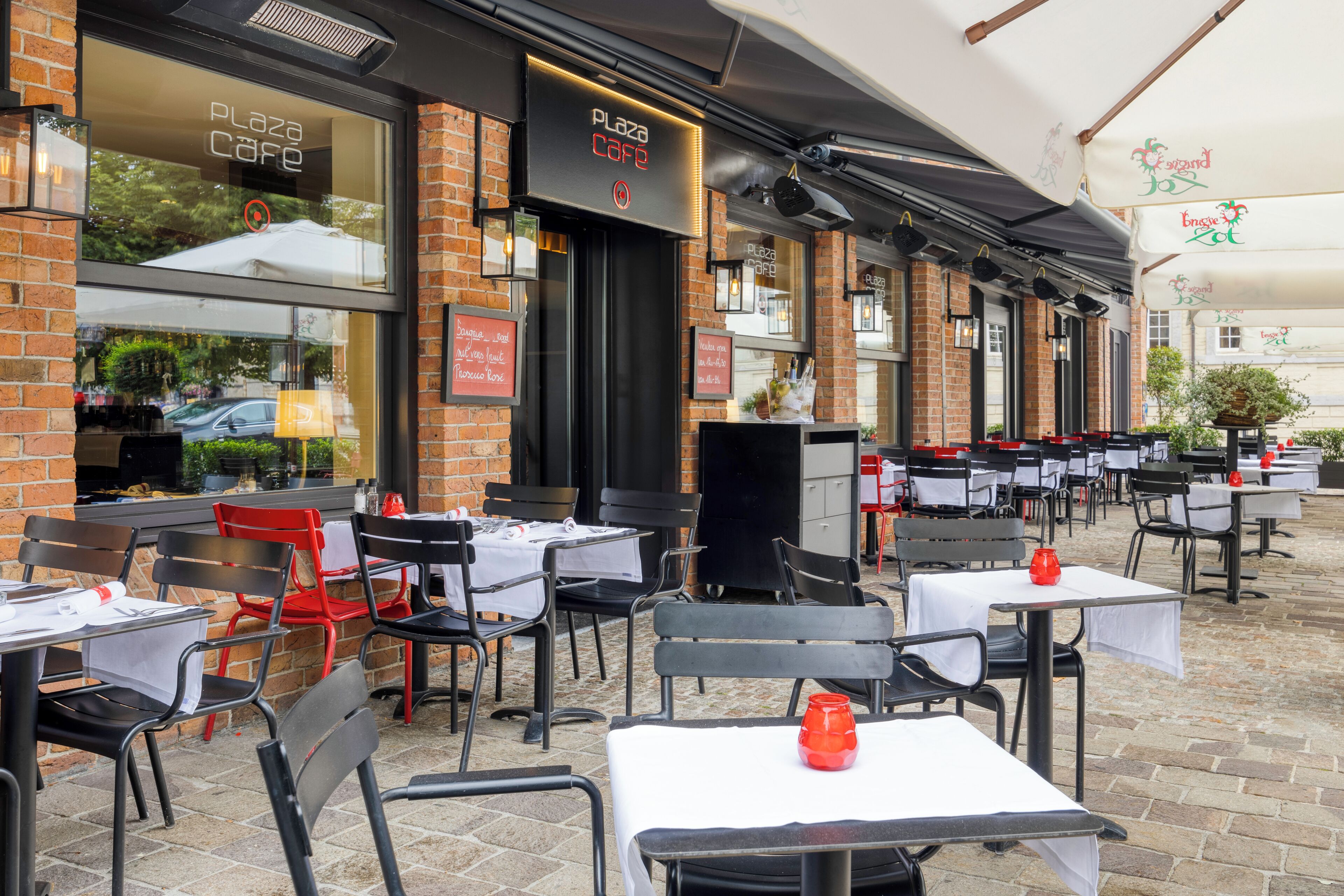 Un café en plein air avec des murs en briques, des tables recouvertes de nappes blanches et des chaises rouges.