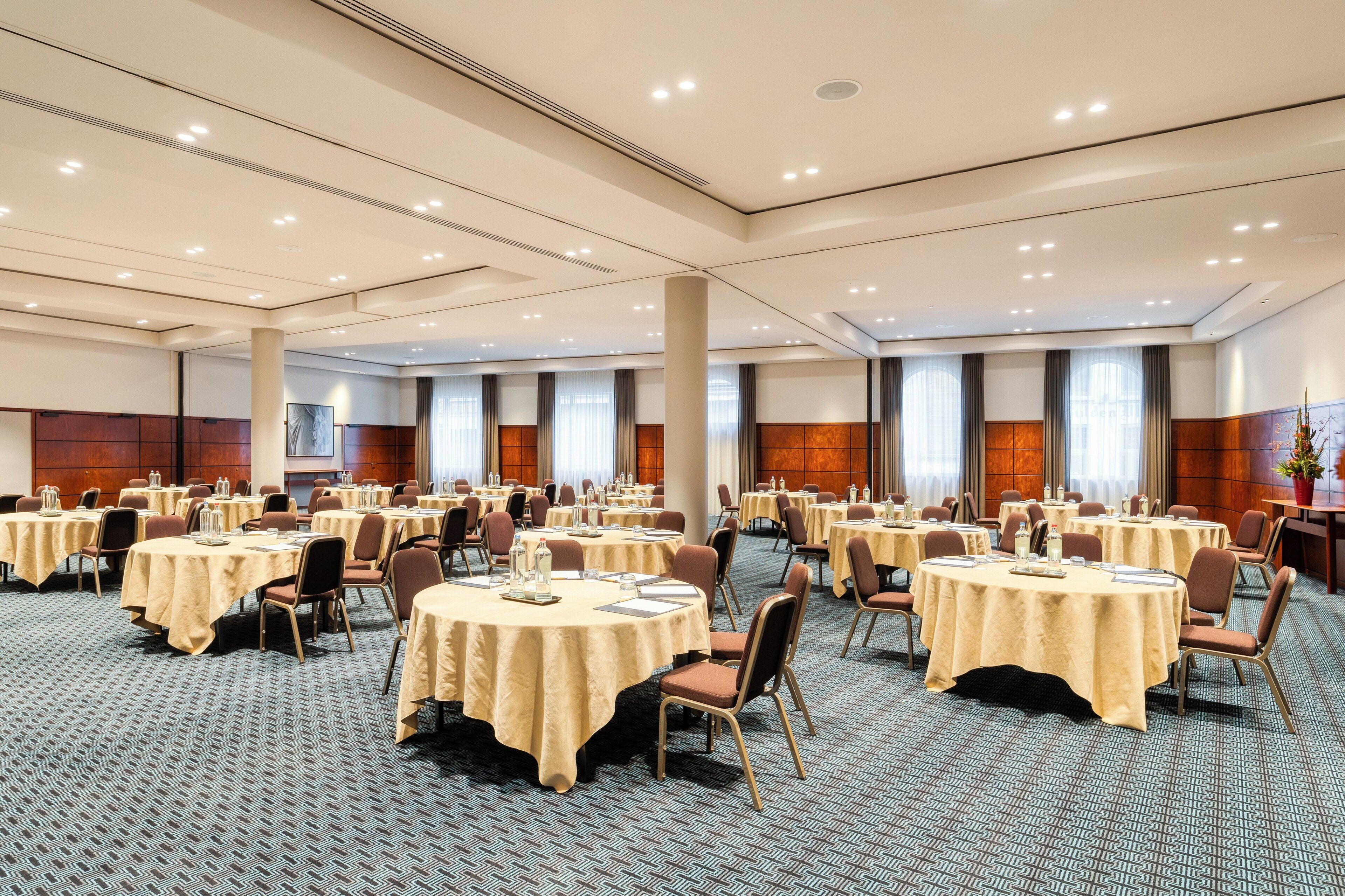 Un amplio salón de conferencias con varias mesas redondas, sillas y piso alfombrado.