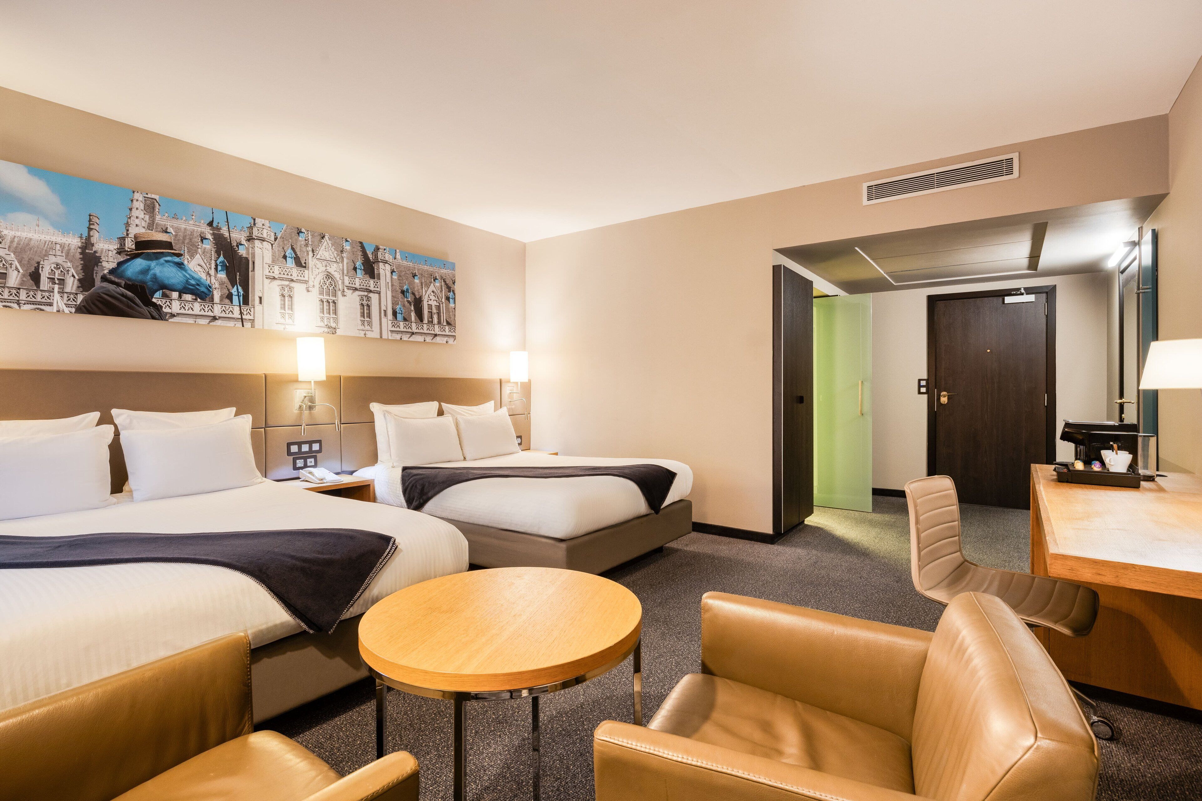 A hotel room with two beds, a round table, leather chairs, a desk, and a painting on the wall.