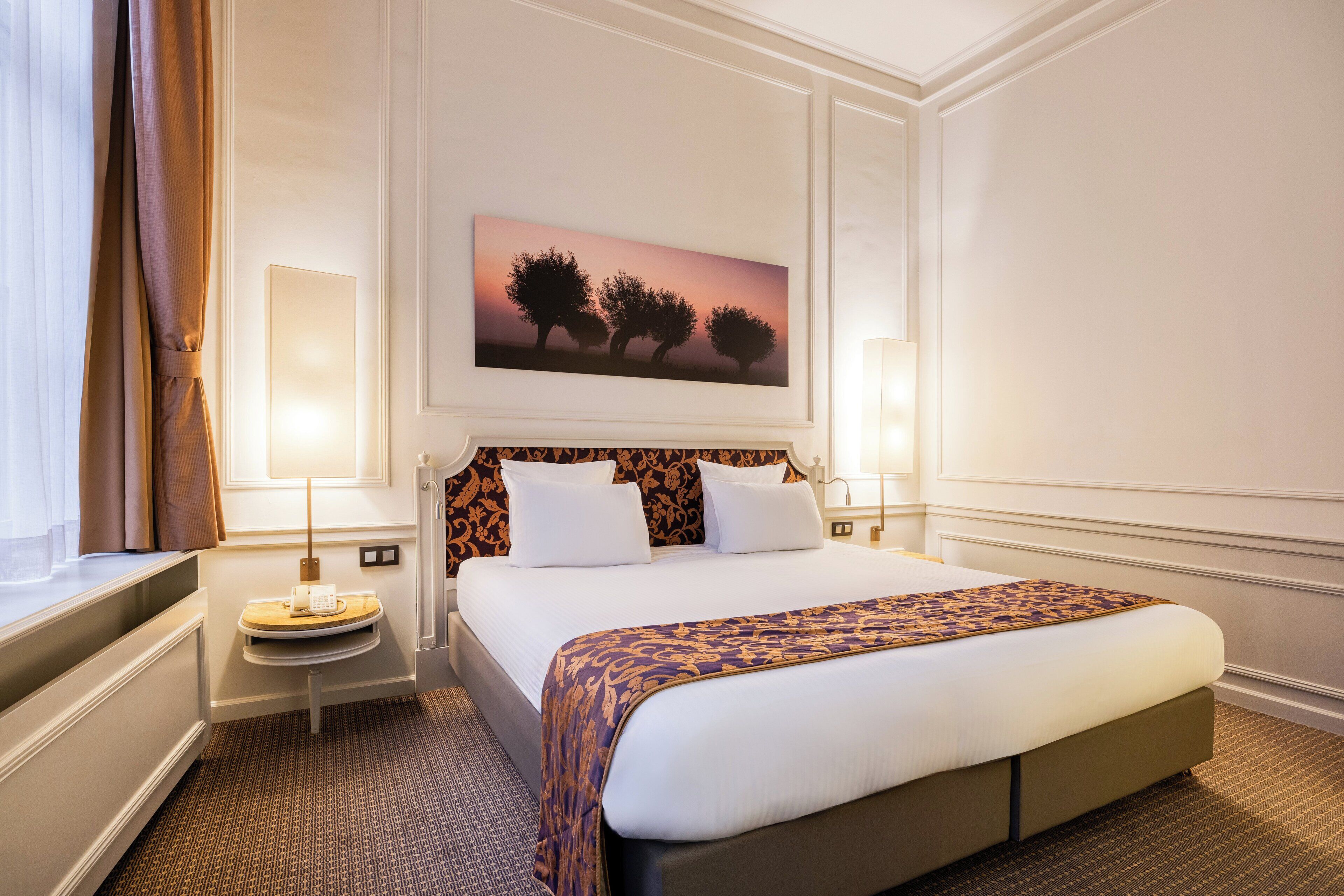 Hotelkamer met een groot bed, een nachtkastje, een wandlamp en een schilderij van bomen.