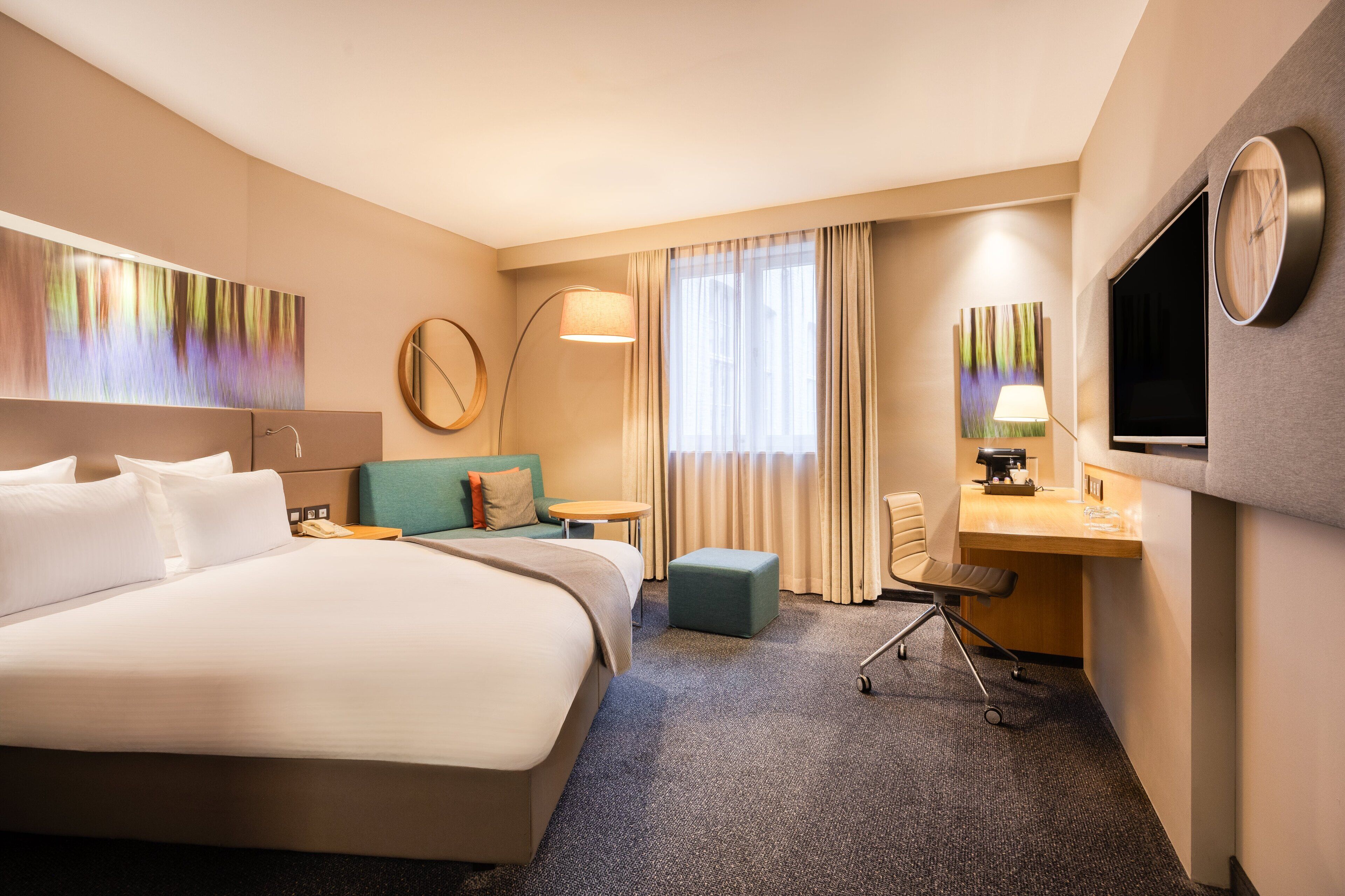 Una habitación de hotel con una cama grande, un escritorio con computadora, una silla, un sofá y un televisor.