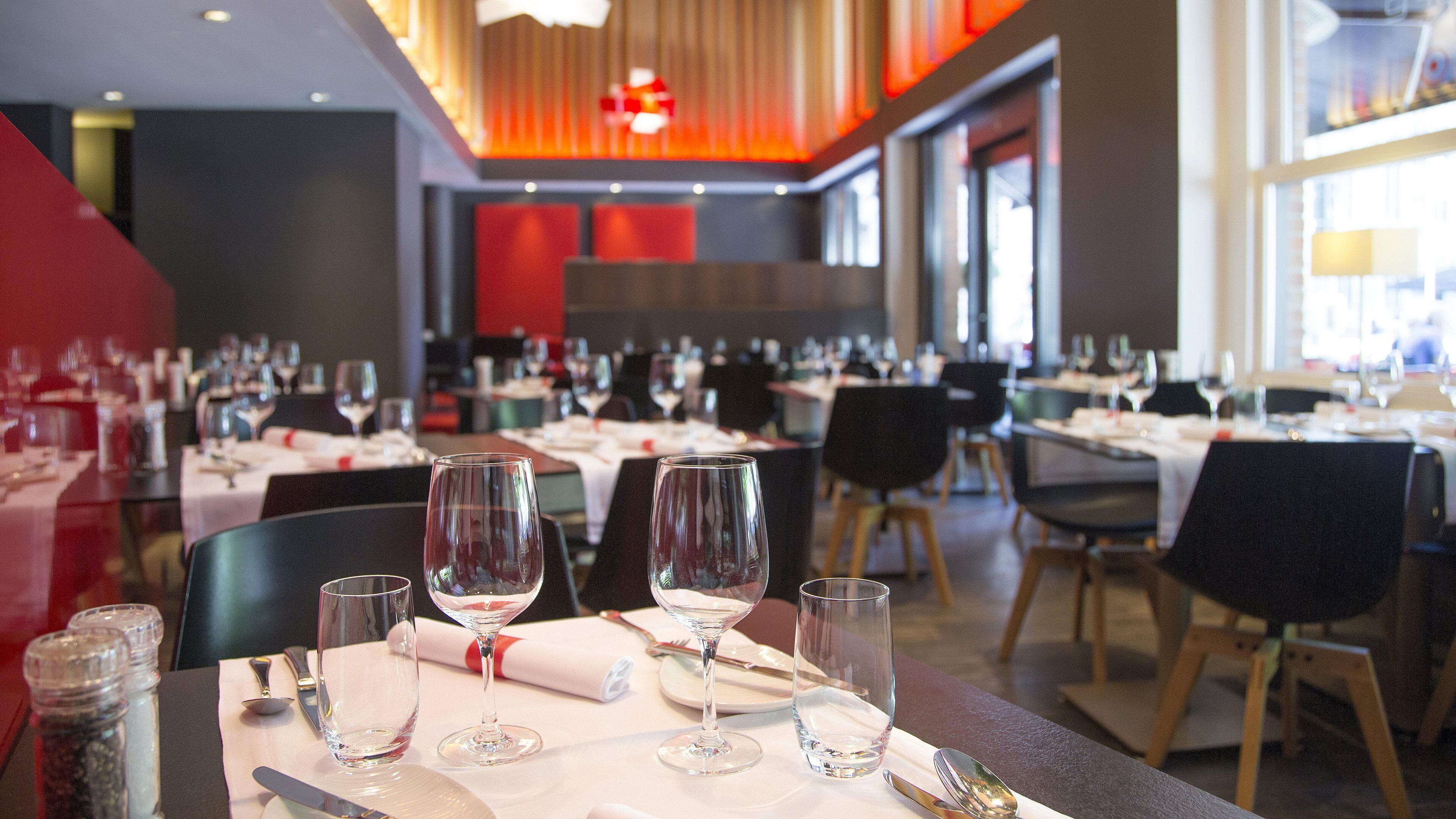 A restaurant with multiple tables set for dining, featuring wine glasses and cutlery.