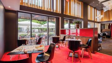 A restaurant with red carpet flooring, modern black chairs, and large windows overlooking an outdoor seating area.