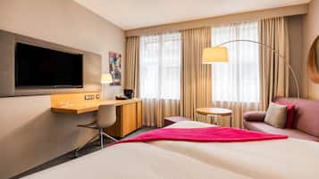 A hotel room with a bed, desk, chair, TV, lamp, and a sofa.