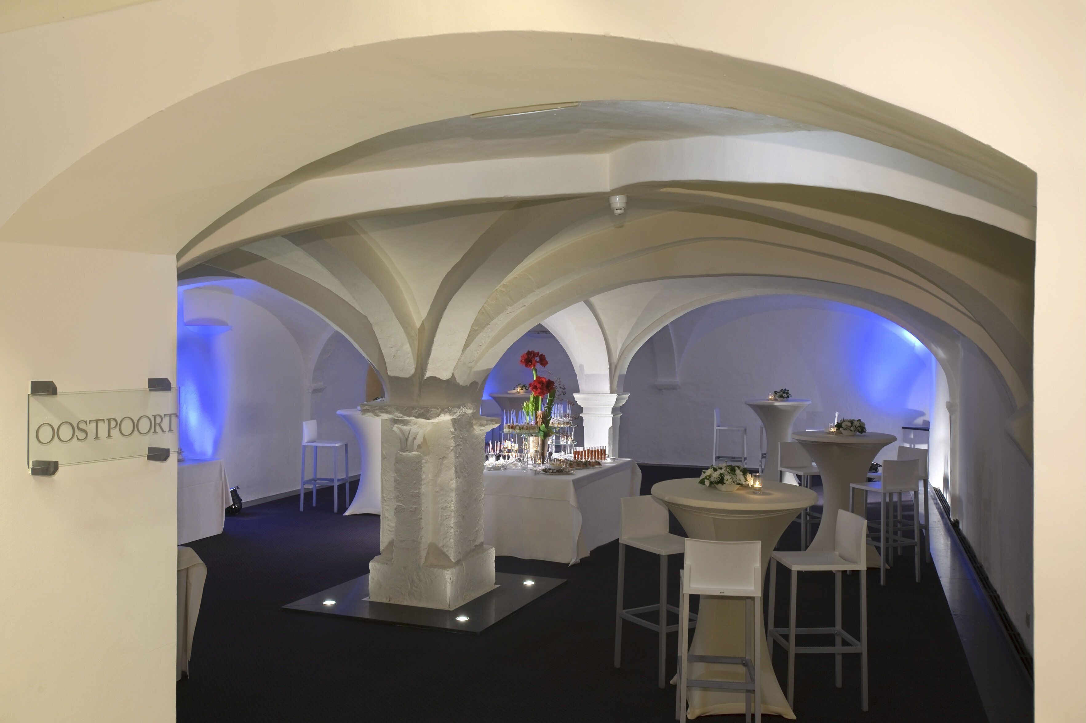 Un interior moderno con techos abovedados, una columna blanca central y mesas con centros de flores.