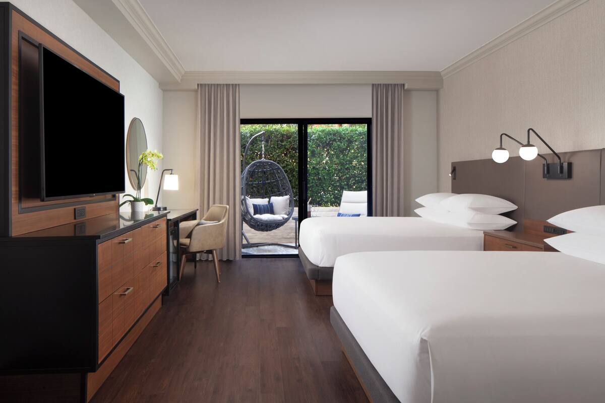A hotel room with two beds, a TV, a desk, and a chair.