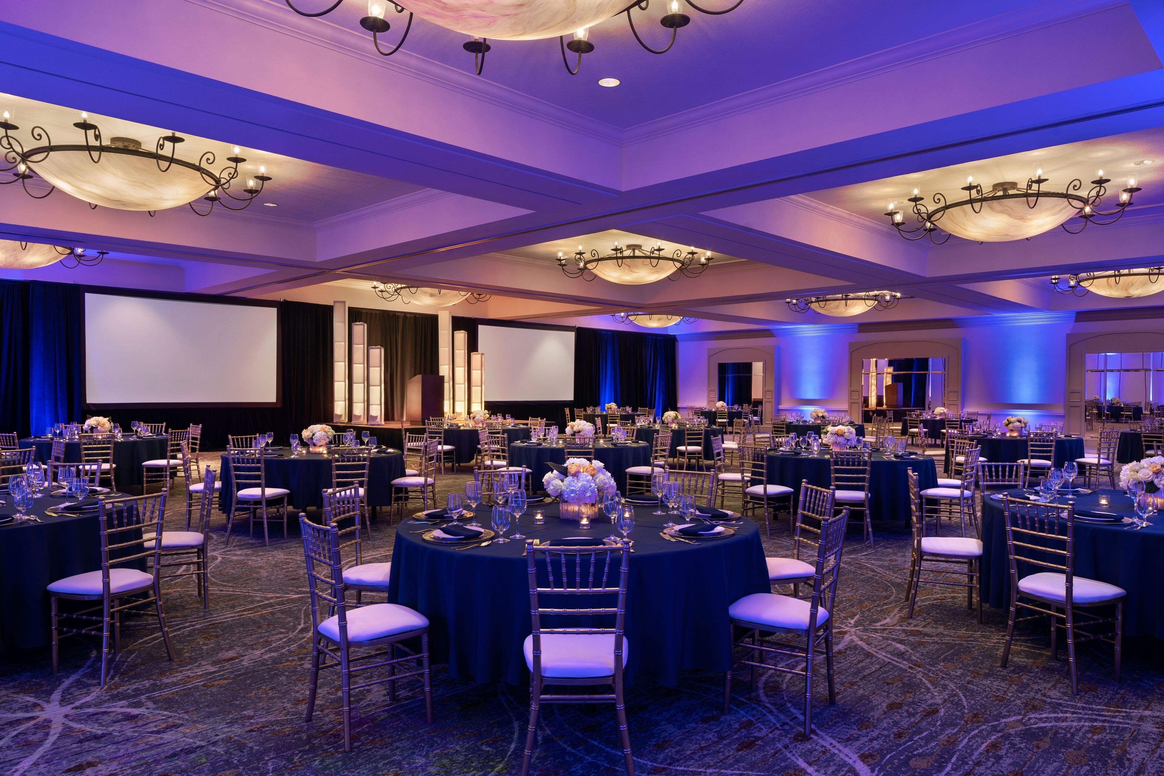 Une salle de banquet avec des tables rondes, des chaises et des lustres.