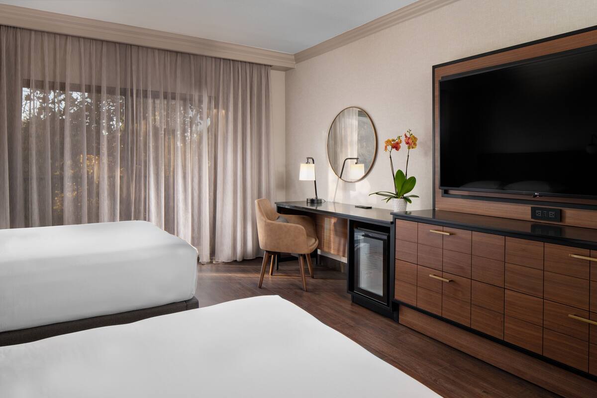 A hotel room with two beds, a desk with a chair, a television, and a mirror.