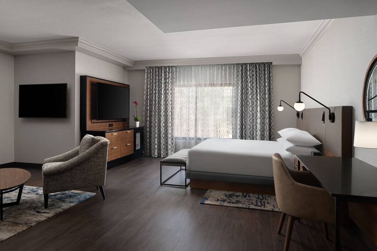 A hotel room with a bed, a desk, a chair, a television, a dresser, and a window with curtains.