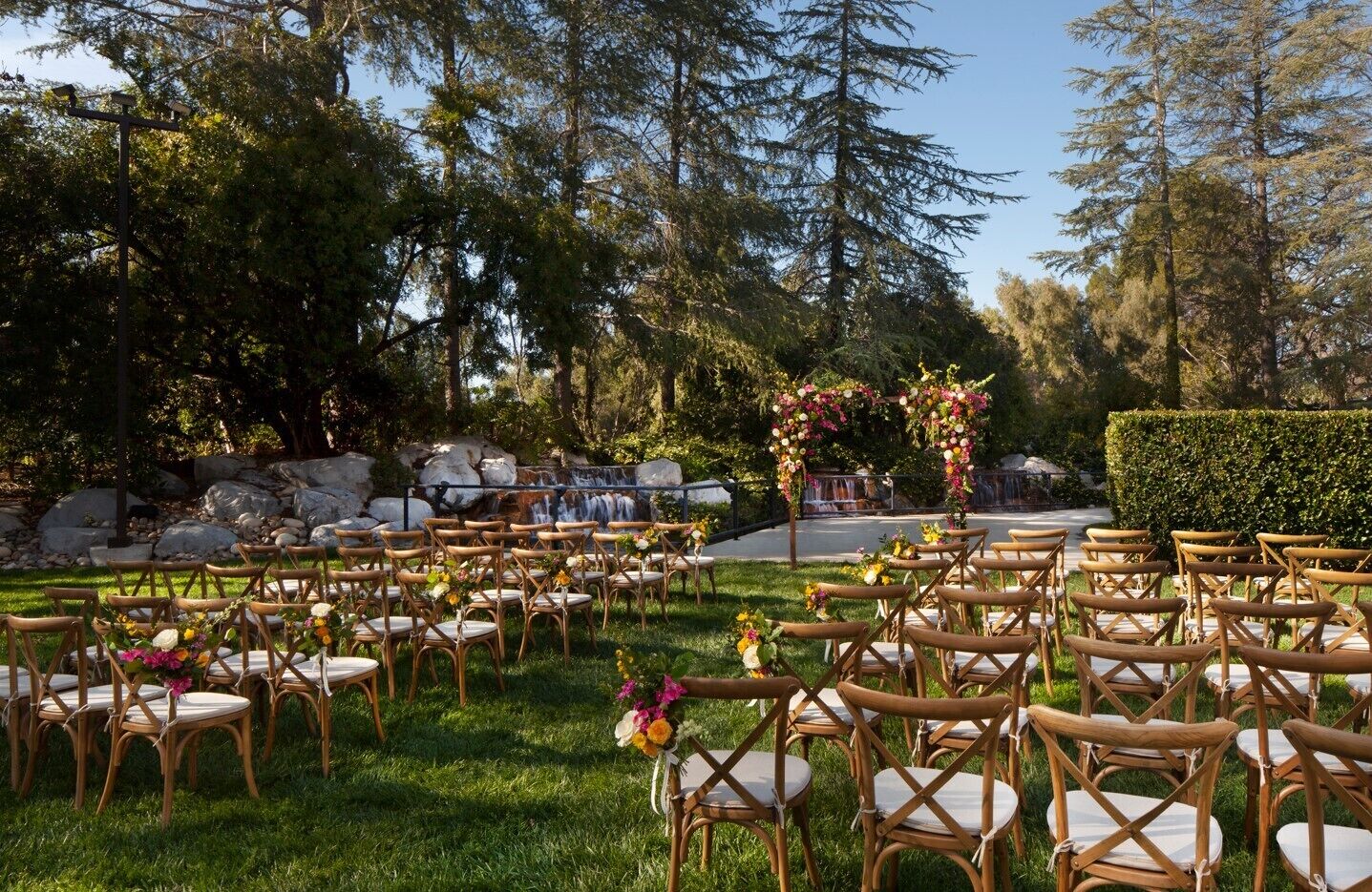 Un lieu de réception en plein air pour les mariages, avec des rangées de chaises en bois et une cascade en arrière-plan.