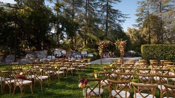 Un lieu de réception en plein air pour les mariages, avec des rangées de chaises en bois et une cascade en arrière-plan.