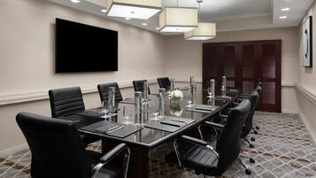 A conference room with a long table, black chairs, a flat-screen TV, and a patterned carpet.