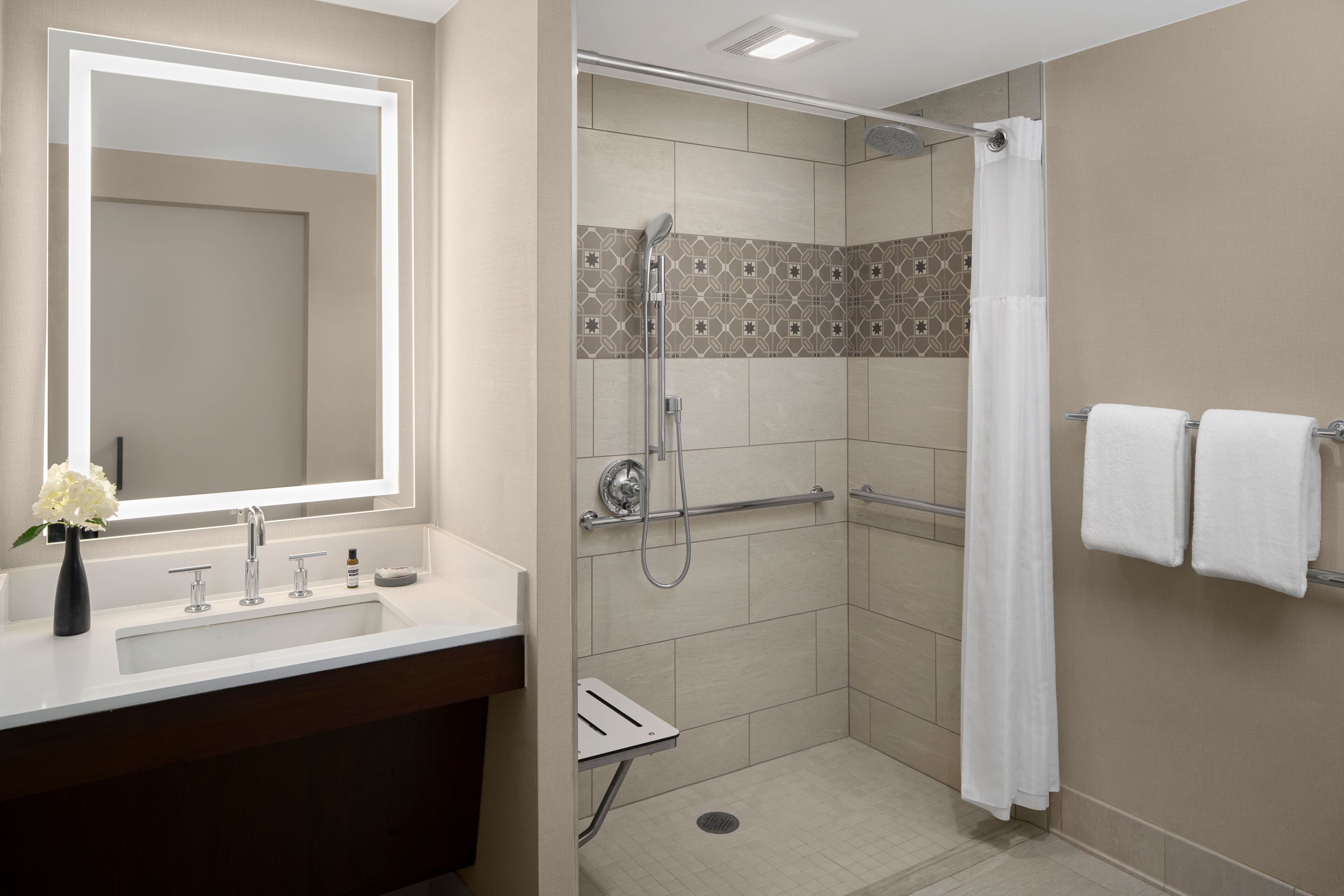 Een moderne badkamer met een grote spiegel, een wastafel, een douche met glazen deur en twee handdoeken op een rek.