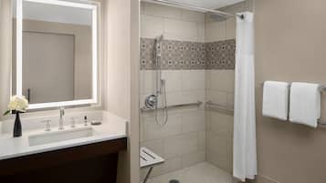 Een moderne badkamer met een grote spiegel, een wastafel, een douche met glazen deur en twee handdoeken op een rek.