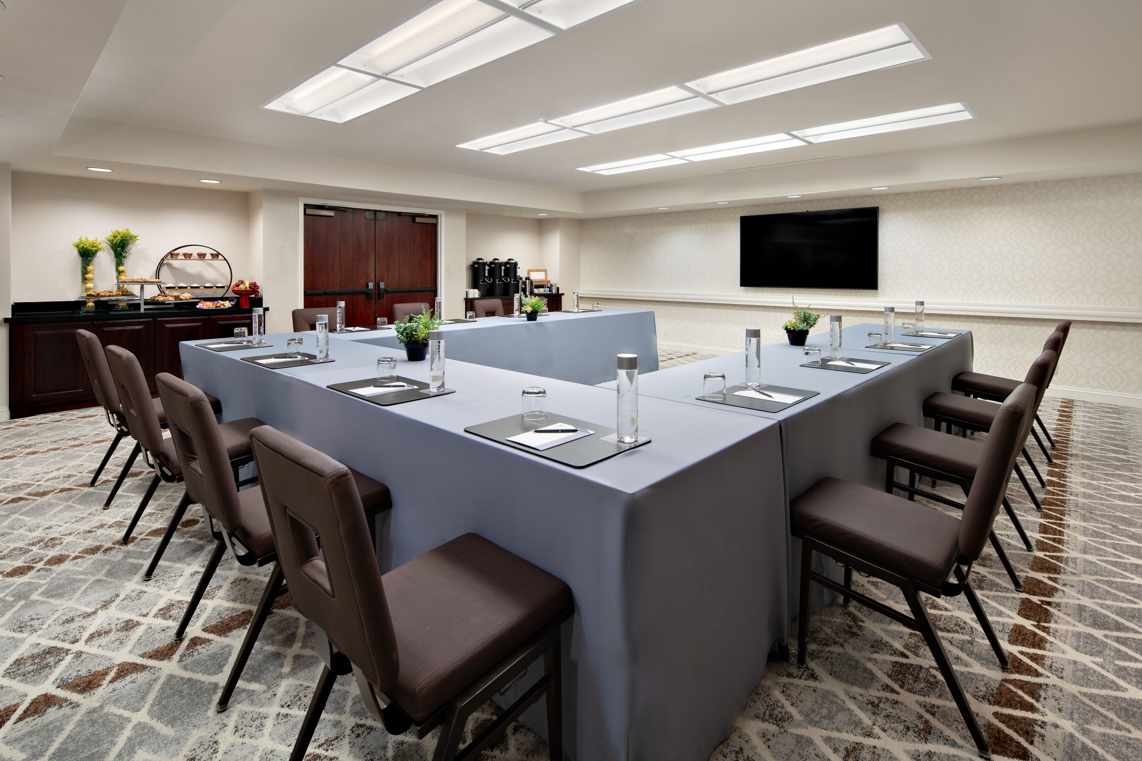 A conference room with a long table, chairs, a TV, and a coffee station.