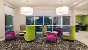 A modern lounge area with colorful chairs, a patterned carpet, and large windows offering a view of the outside. - La Quinta Inn & Suites by Wyndham Mobile (Mobile)
