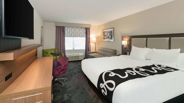 A hotel room with a large bed, a desk, a television, a window with curtains, a small table, and a chair. - La Quinta Inn & Suites by Wyndham Mobile (Mobile)