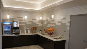 A modern kitchen with a built-in coffee machine, a beverage dispenser, and a fruit basket. - La Quinta Inn & Suites by Wyndham Mobile (Mobile)