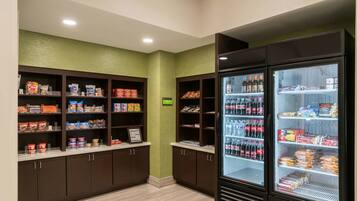 Un espacio de comida autoservicio con dispensadores de bebidas refrigeradas y estantes llenos de aperitivos y bebidas.